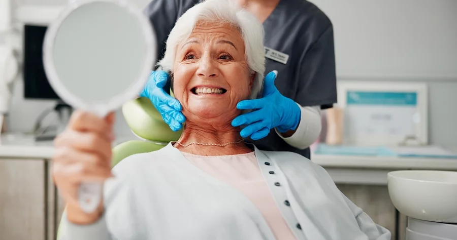 Older woman looking at new dental implants in a mirror
